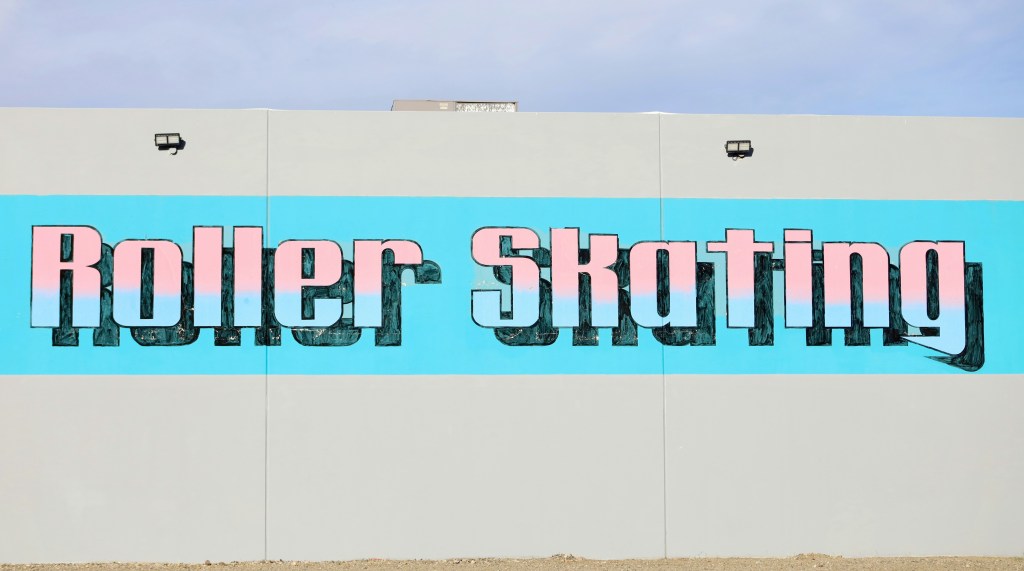 A photograph of the words "Roller Skating" in light pink & blue painting on the side of Roller Kingdom in Reno, NV in daylight. Photo by Manny Becerra